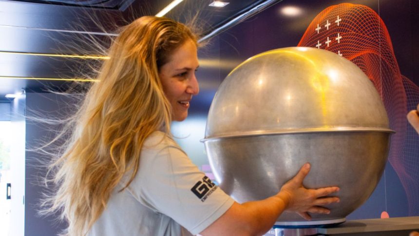 Visitantes participam de demonstração científica com gerador de Van de Graaff em exposição interativa.